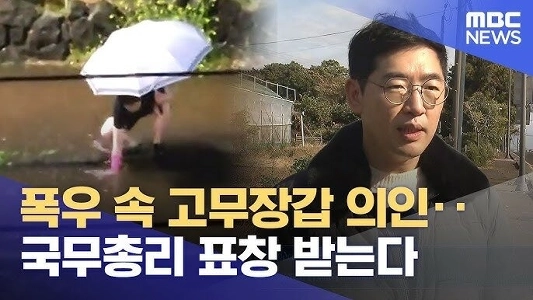 大雨の中、ゴム手袋をした男性が首相から表彰を受ける。